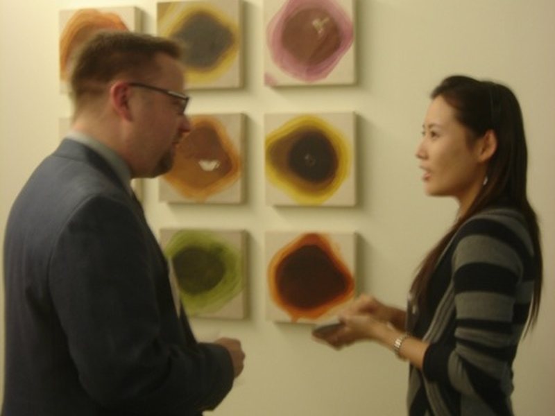 The artist discussing the nine-panel Daily Life grid with a visitor at an exhibition